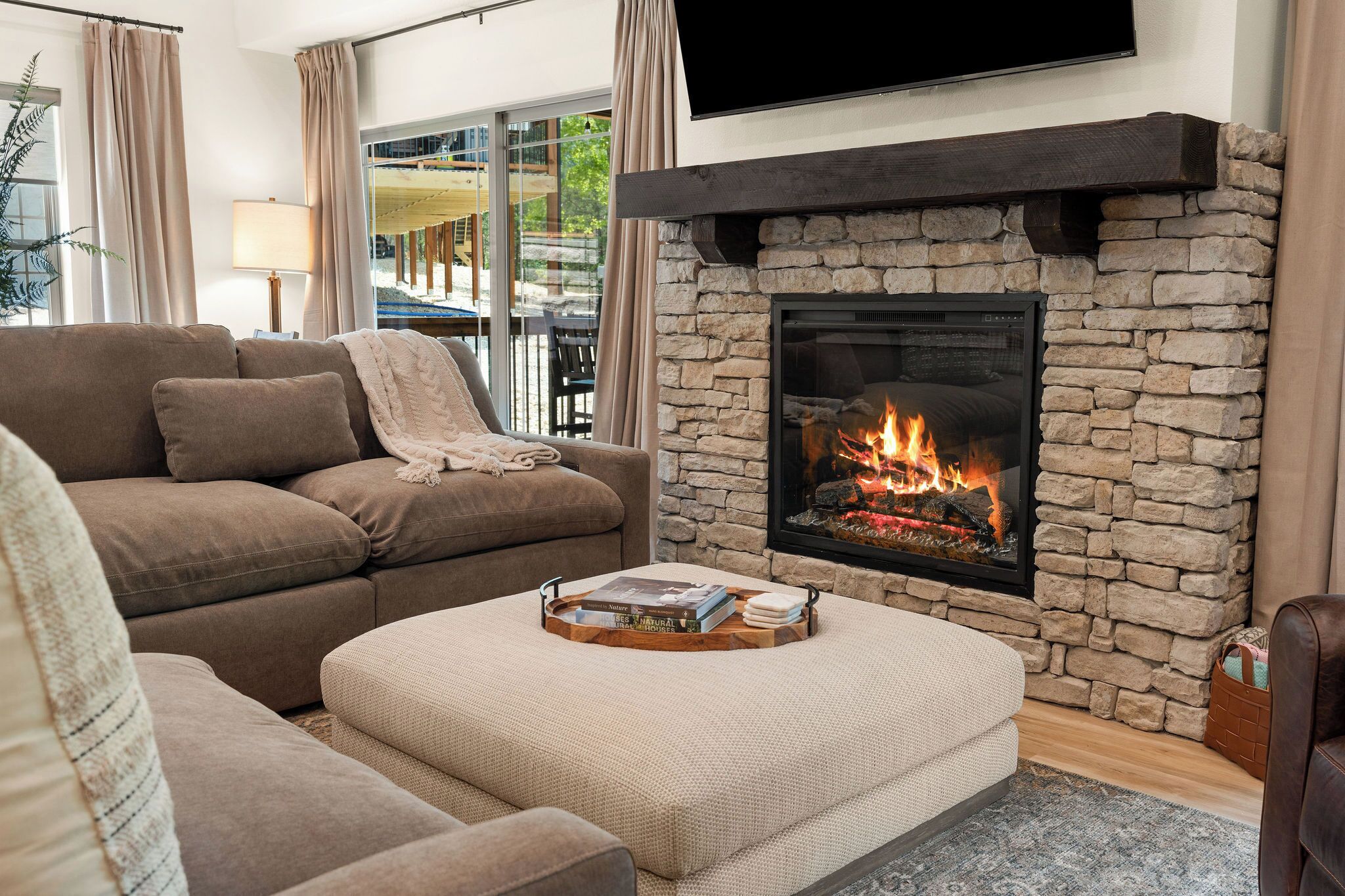 Ein Wohnzimmer mit Kamin aus Stein, einer Couch, einem Couchtisch mit Büchern und einem Fernseher, der über dem Kamin angebracht ist.