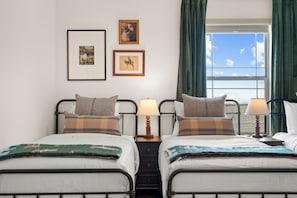 Ein Hotelzimmer mit zwei Betten, einem Nachttisch mit Lampen und gerahmten Bildern an der Wand.