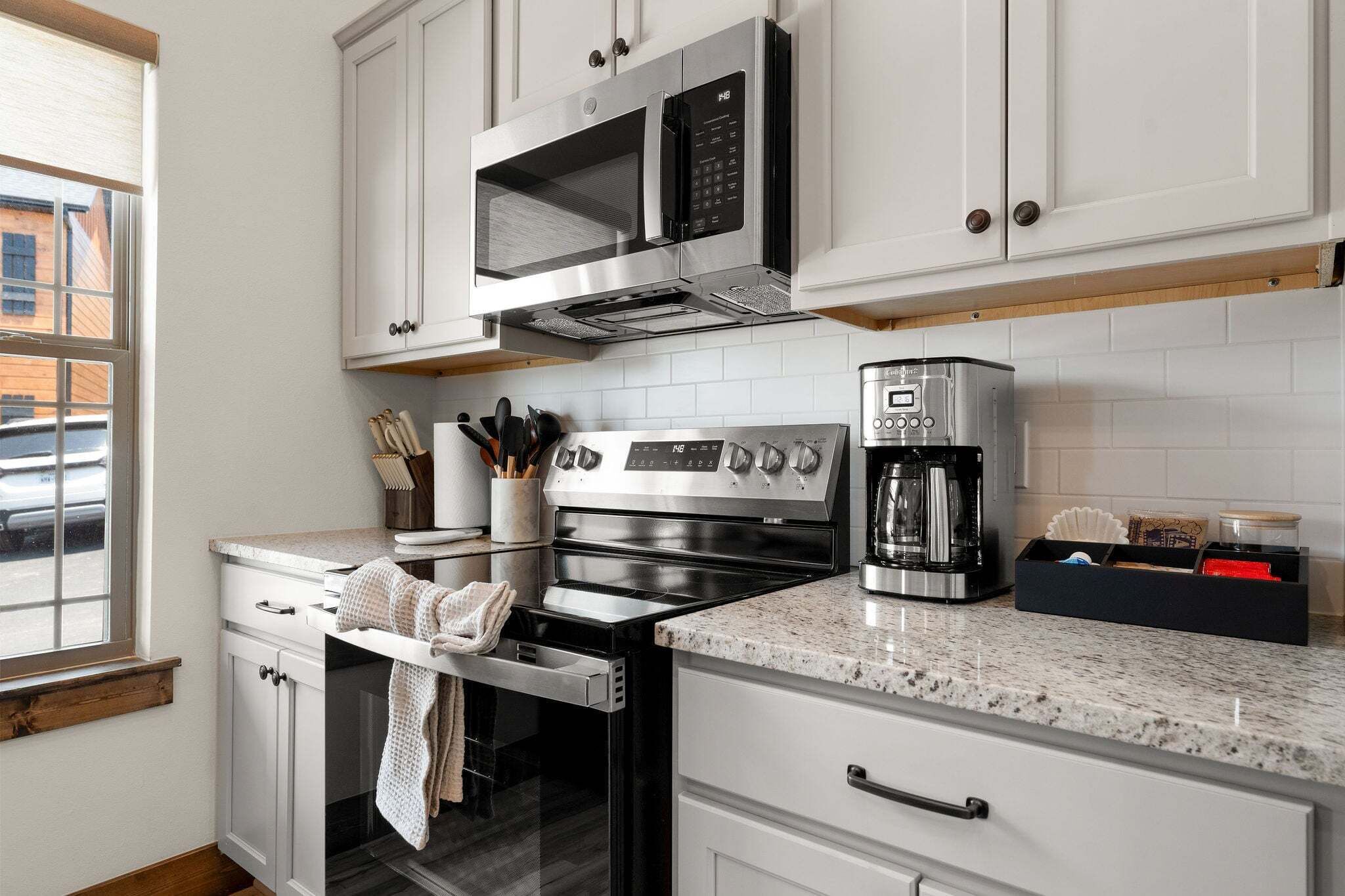 A kitchen with white cabinetry, a stainless steel oven, a microwave, and a coffee maker.