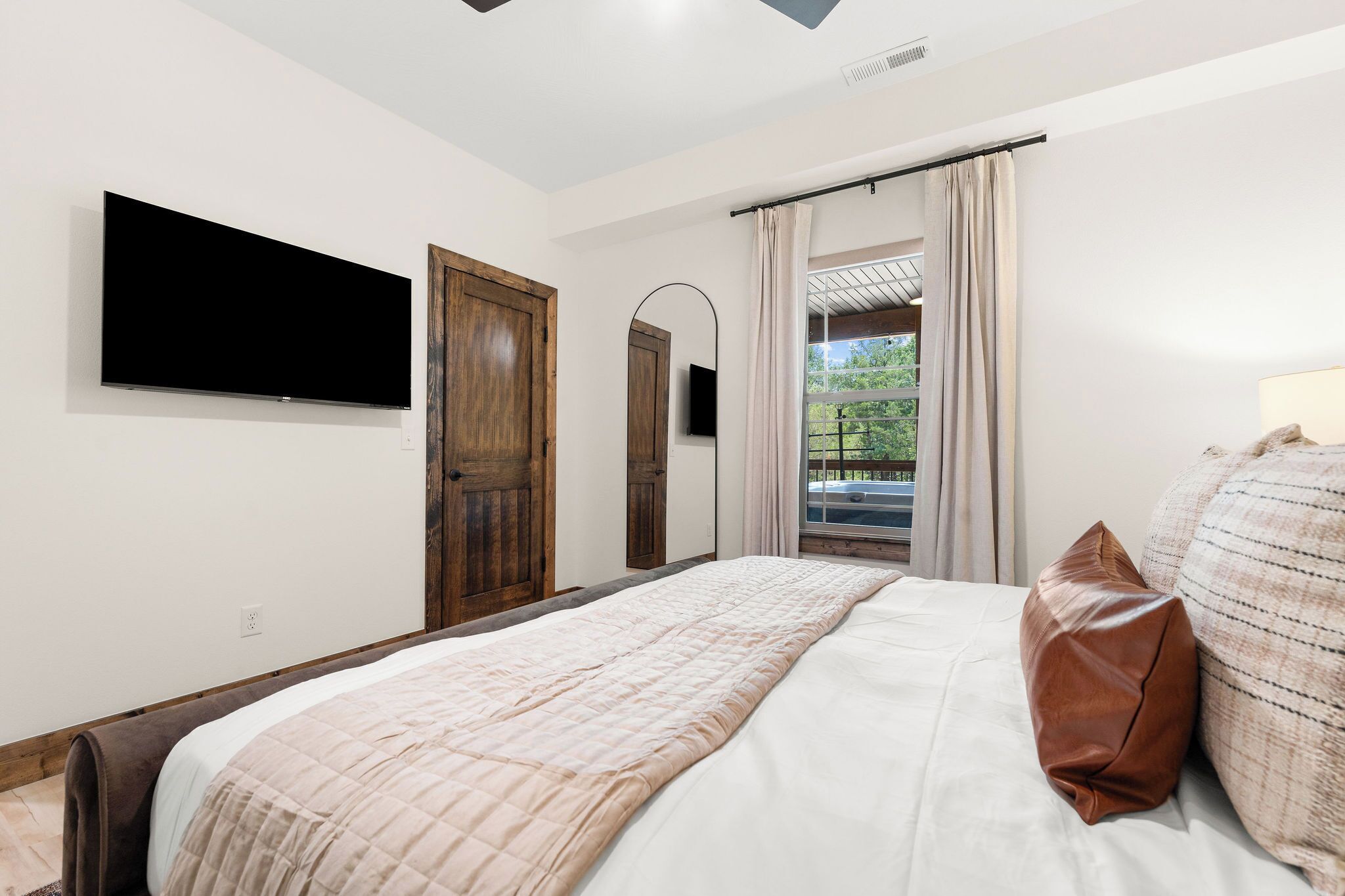 Ein Schlafzimmer mit Bett, einem an der Wand montierten Fernseher und Blick ins Freie durch ein Fenster.