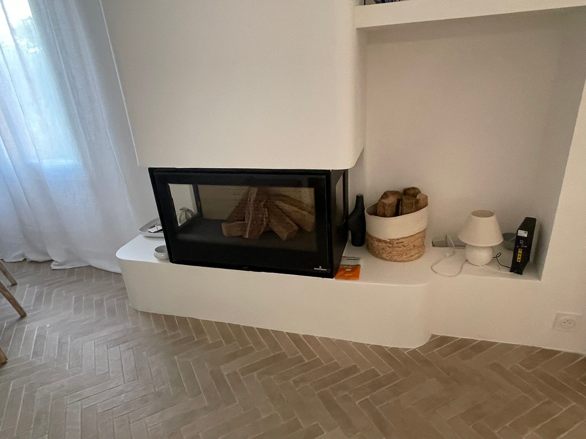 Ett modernt vardagsrum med en inbyggd öppen spis, en vit hylla med dekorativa föremål och ett golv med fiskbensmönster.