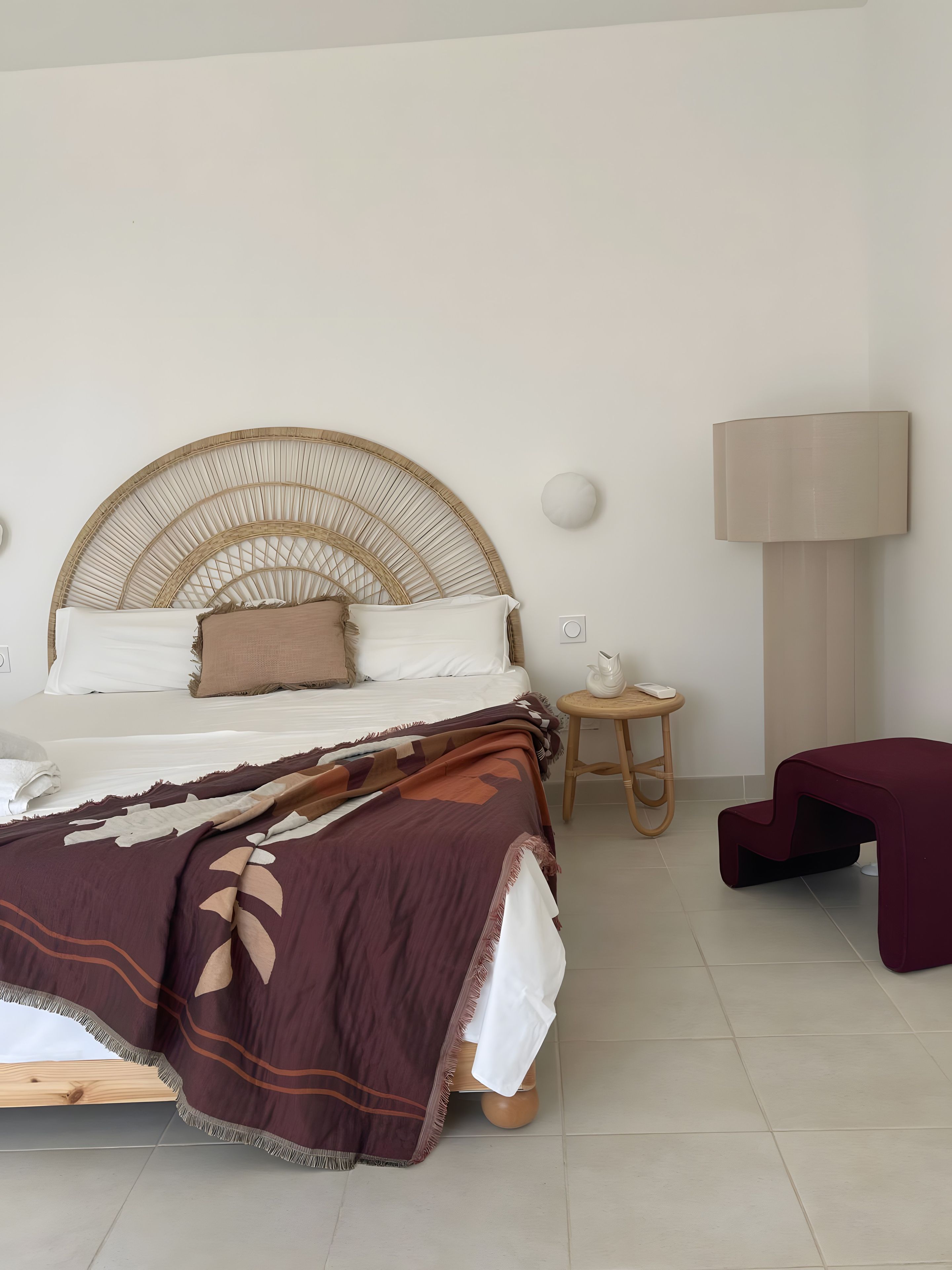 A bed with a woven headboard, a bedside table with a lamp, and a bench.