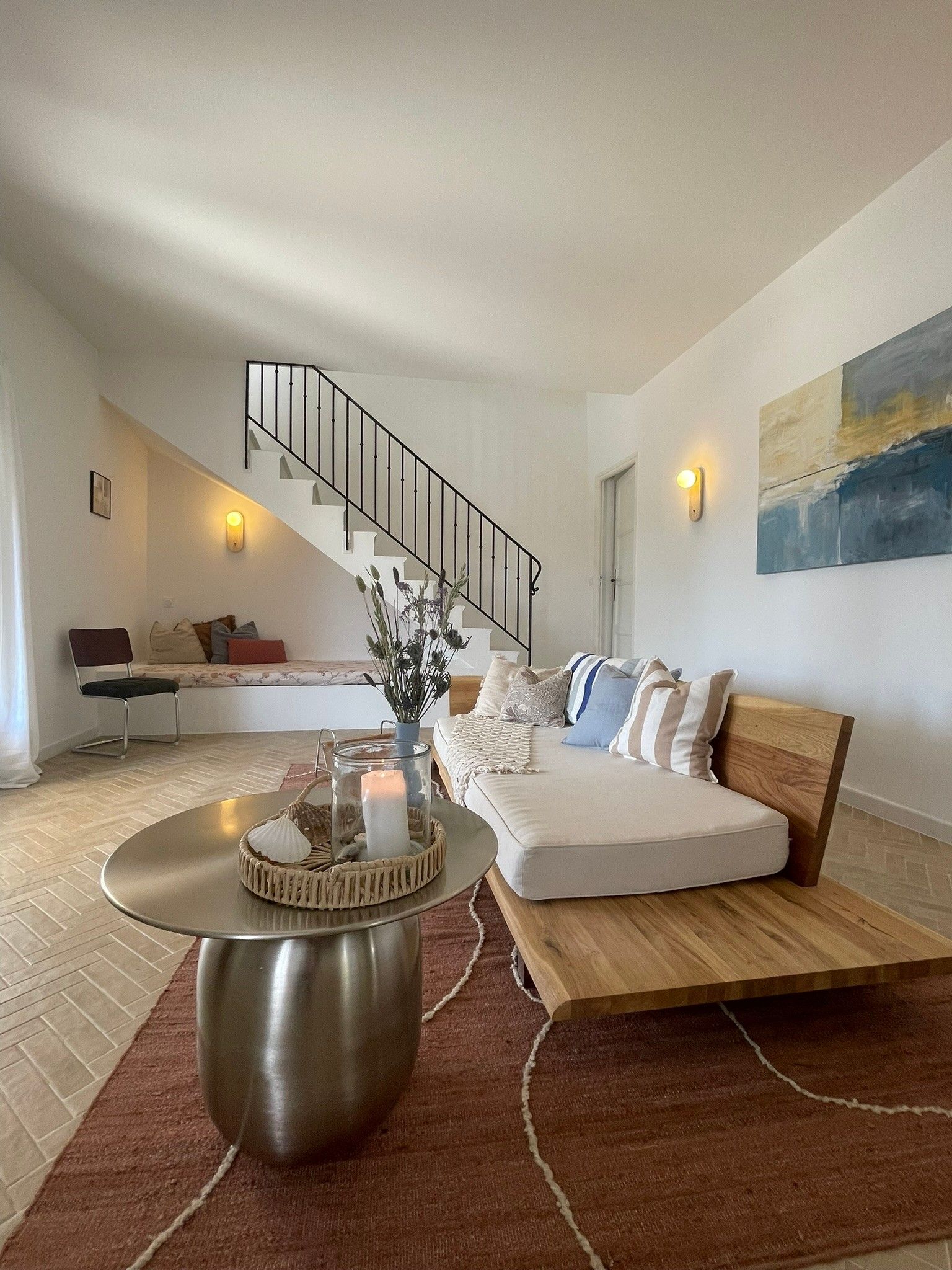 A modern living room with a staircase, a sofa set, a coffee table, and a painting on the wall.