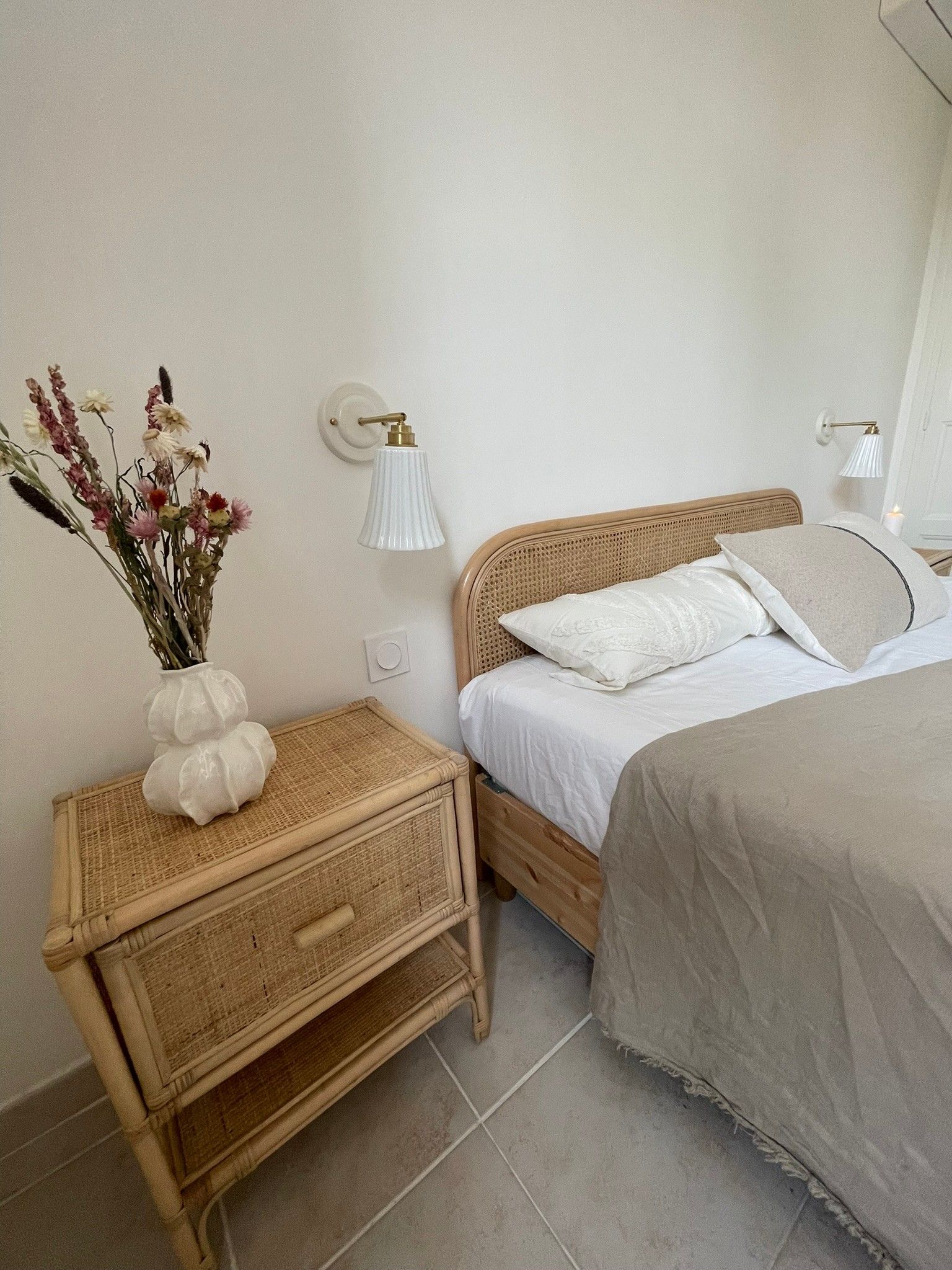 A bedroom with a bed, bedside tables, a lamp, and a vase with flowers.