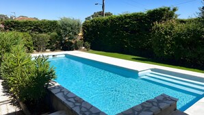 A rectangular swimming pool with a stone border, surrounded by lush greenery and a clear blue sky. - 4-Bedroom Villa with Private Pool near the Sea, Wi-Fi, and Air Conditioning (Saint-Raphaël)