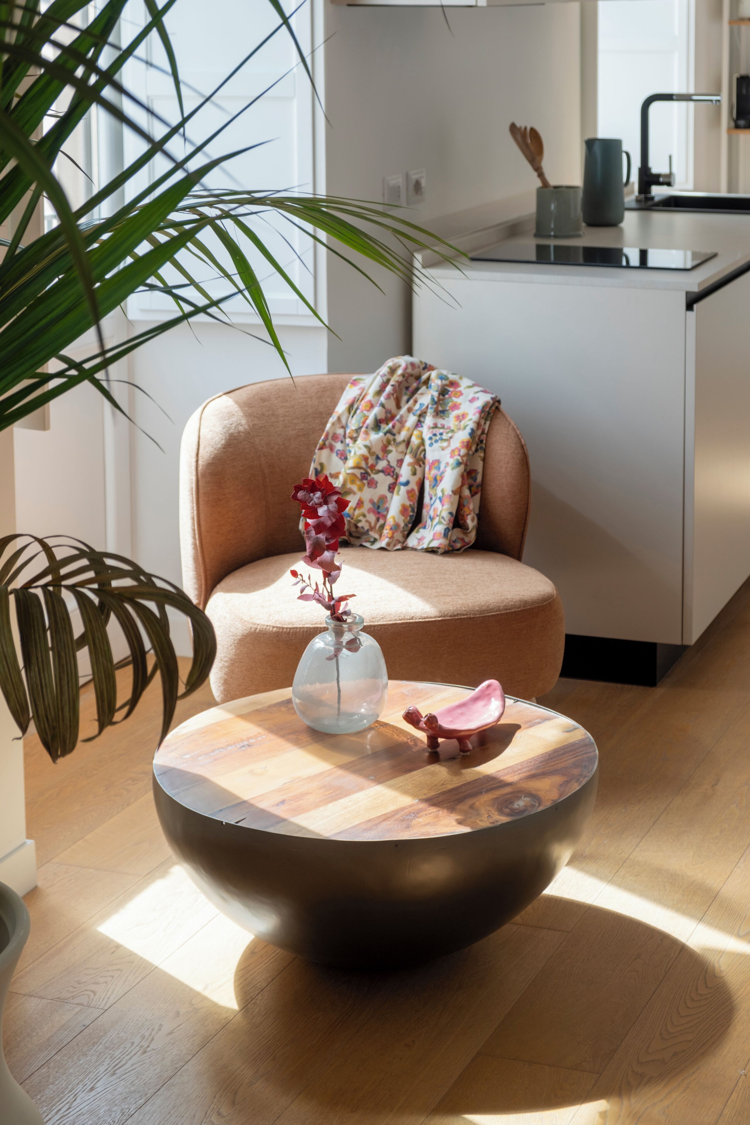 A modern kitchen with a round wooden coffee table, a chair with a floral cushion, and a potted plant.