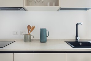 A modern kitchen with a black sink, a blue mug, and a wooden spoon in a green mug. - Palazzo Valguarnera Luxury Apartments (Palermo)