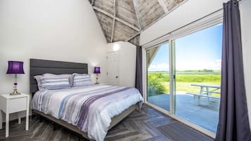 A bedroom with a bed, nightstands, a window, and a view of a grassy field.