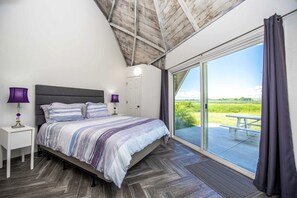 Un dormitorio con cama, mesitas de noche, una ventana y vistas a un campo cubierto de hierba.