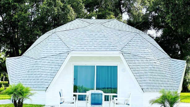 A geodesic dome structure with a patio area, outdoor seating, and a view of the surrounding greenery.