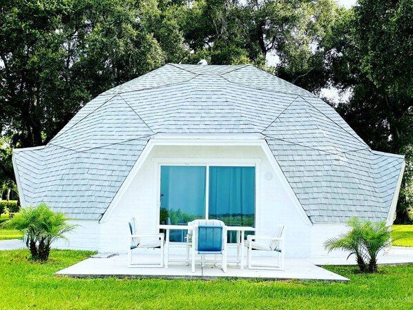 A geodesic dome structure with a patio area, outdoor seating, and a view of the surrounding greenery.