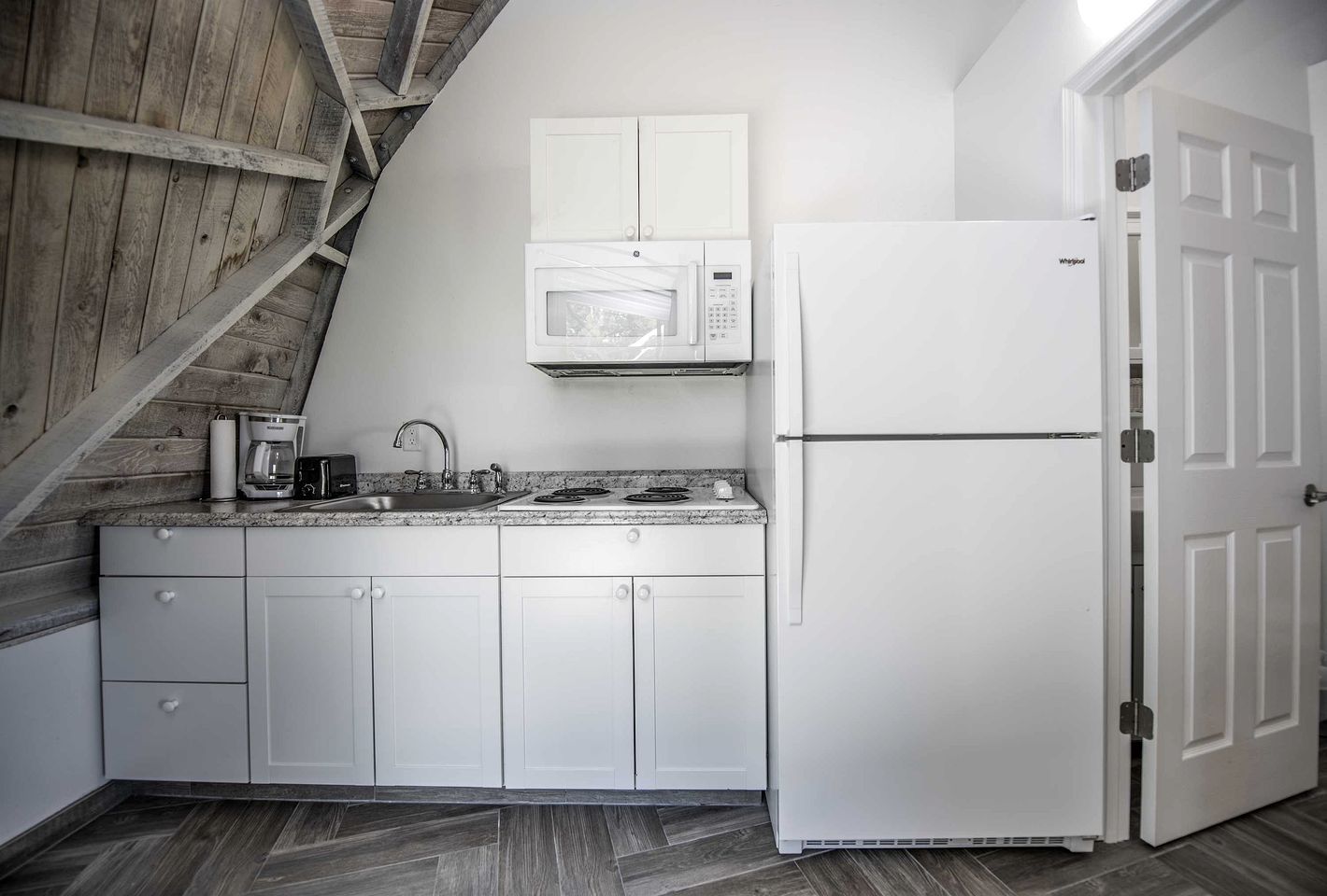A kitchen with white cabinets, a microwave, a refrigerator, a coffee maker, and a sink.