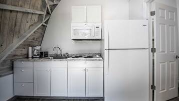 A kitchen with white cabinets, a microwave, a refrigerator, a coffee maker, and a sink.