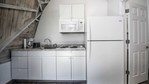 A kitchen with white cabinets, a microwave, a refrigerator, a coffee maker, and a sink.