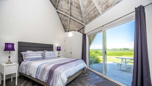 A bedroom with a bed, nightstands, a window, and a view of a grassy field.