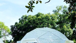 A dome-shaped building with a white exterior and large windows, surrounded by greenery.