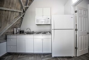 Cozinha com armários brancos, micro-ondas, frigorífico, máquina de café e pia.