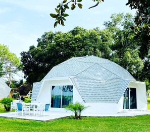 Un edificio a forma di cupola con esterno bianco e ampie finestre, circondato dal verde.