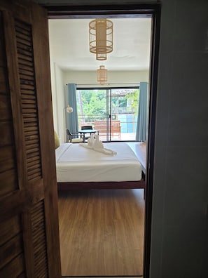 A bedroom with a bed, a wooden floor, a ceiling light fixture, and a view of an outdoor area with a table and chairs. - The Last Paradise (Ko Lanta)