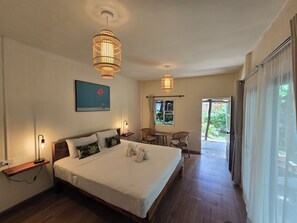 A hotel room with a large bed, bedside lamps, a dining area with chairs, and a view of greenery outside. - The Last Paradise (Ko Lanta)