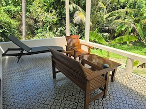 A balcony with a patterned floor, two wooden chairs, a small table, and a lounge chair. - The Last Paradise (Ko Lanta)