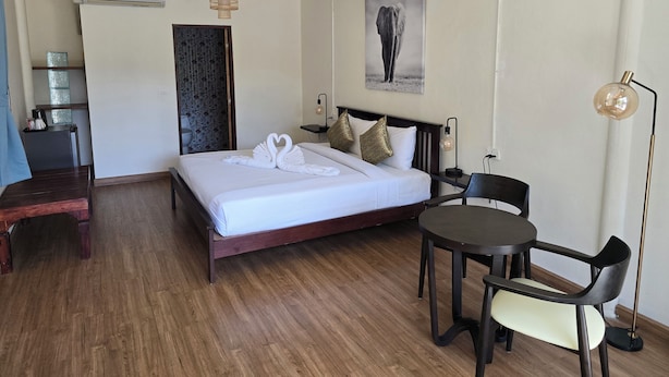 Habitación de hotel con cama, mesita de noche, silla y una pequeña mesa con lámpara.