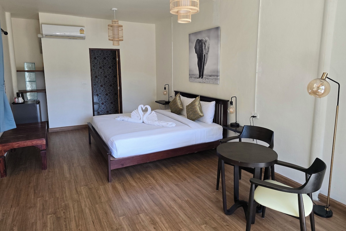 A hotel room with a bed, bedside table, chair, and a small table with a lamp.
