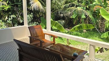 A wooden bench and table set on a patterned floor, with a view of lush greenery and a covered area.