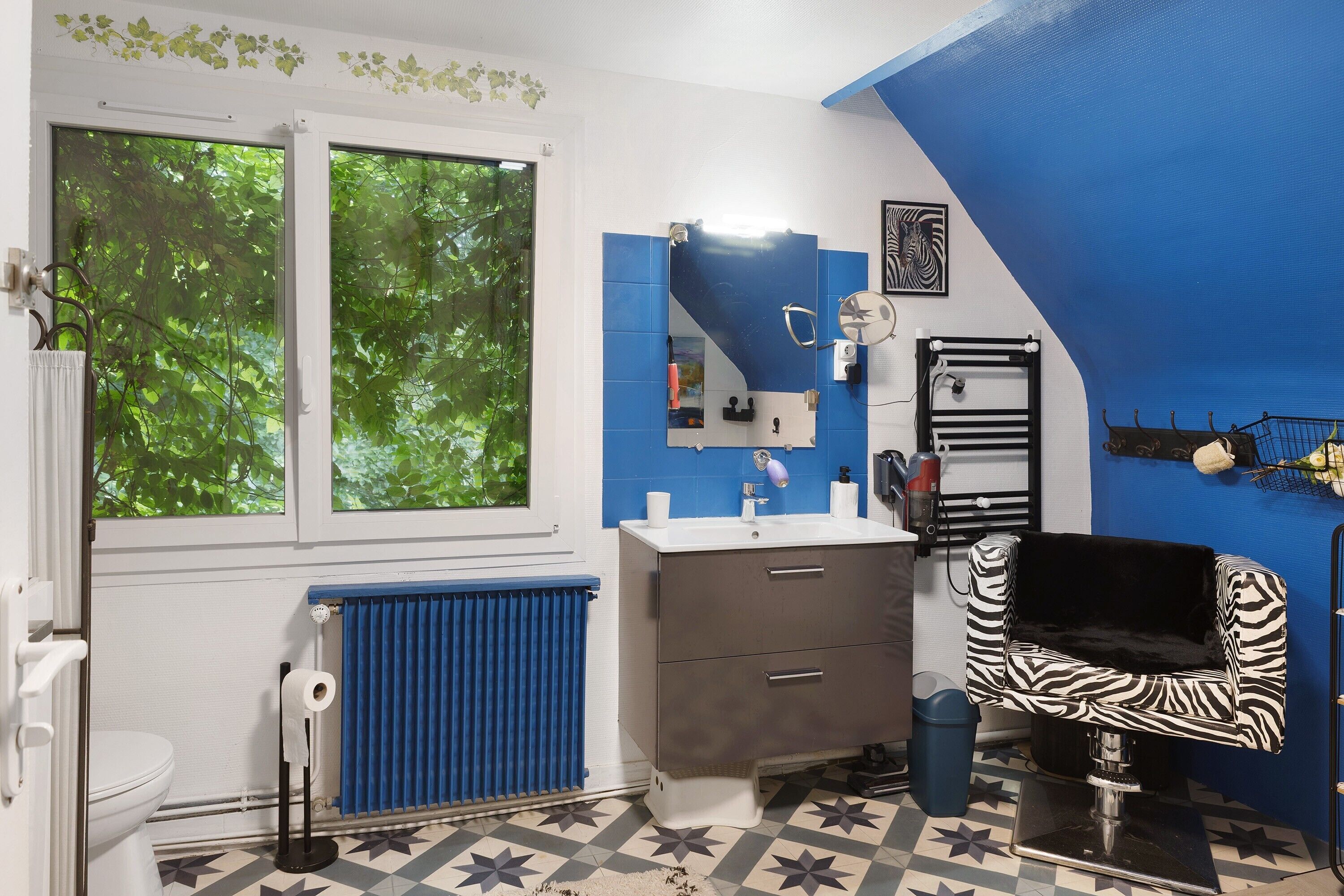 Et badeværelse med et vindue, en radiator, en vask, et spejl og en stol med zebra-mønster.