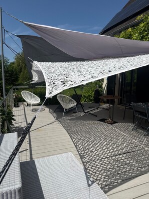 Een terras met een groot wit zonnescherm, tuinmeubilair en een vloer met een patroon.