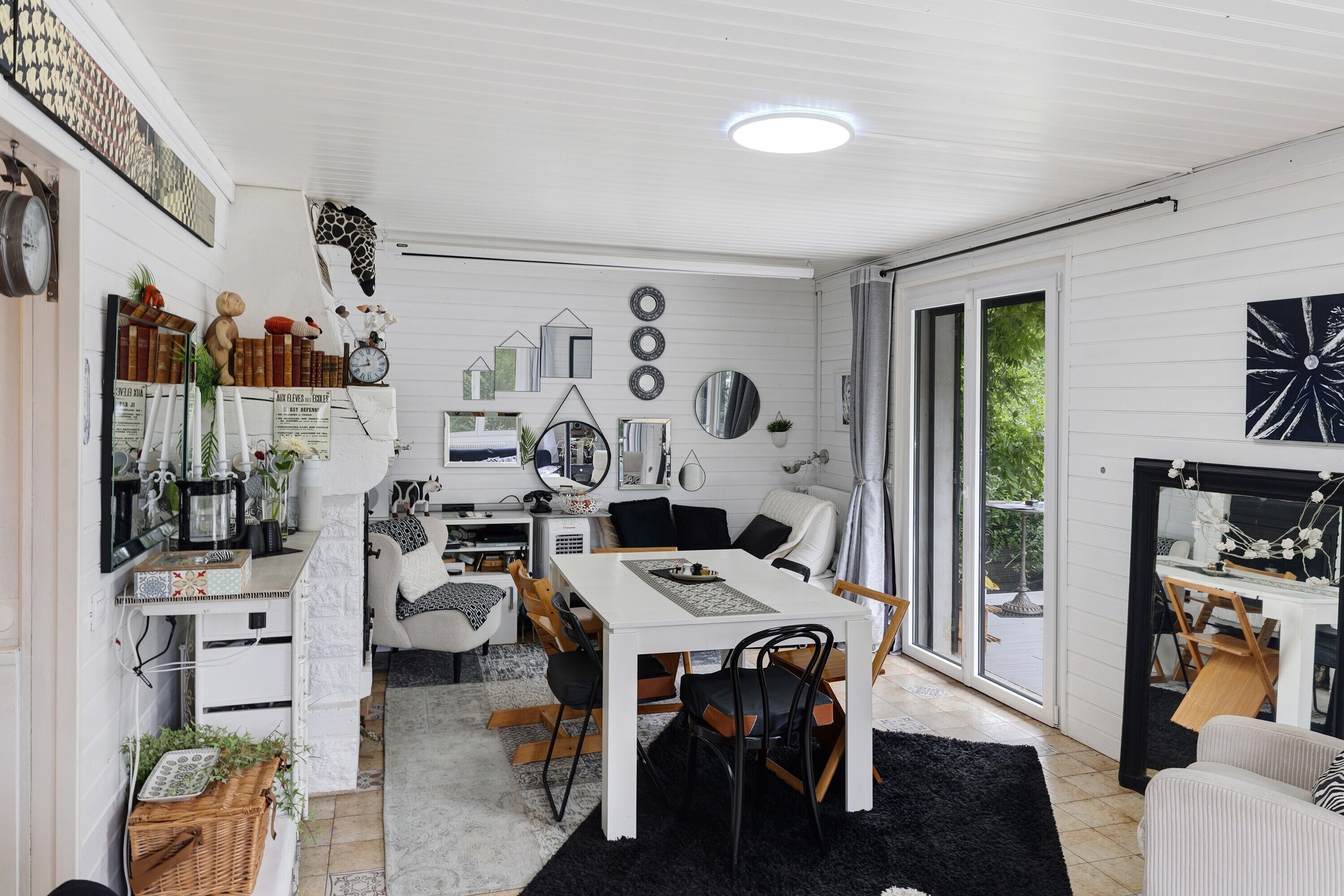 A modern living room with a white ceiling, a dining area with a white table, and a large window.