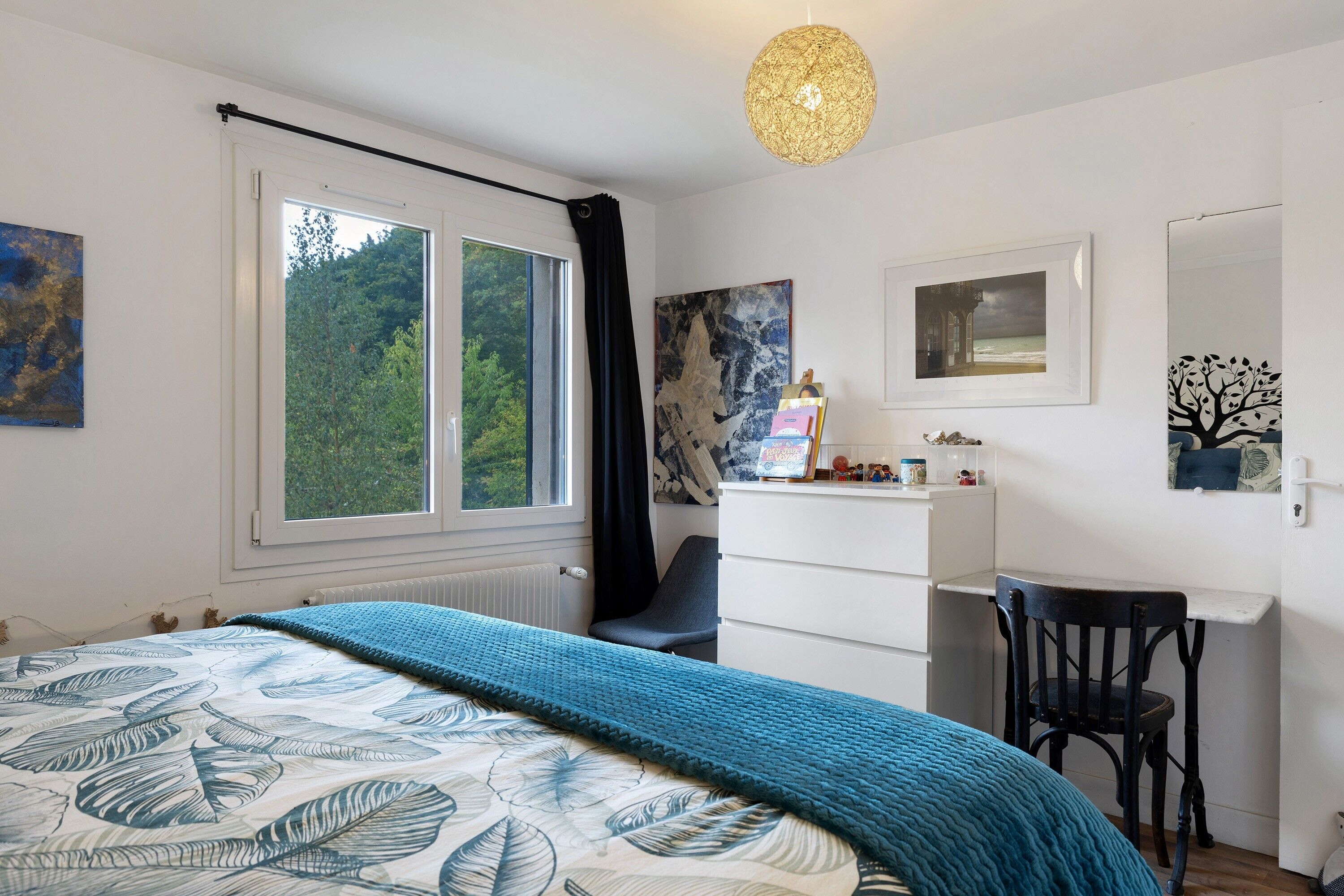 Ein Schlafzimmer mit einem Bett, einem Schreibtisch, einem Stuhl, einem Heizkörper und einem fenster mit Vorhängen.