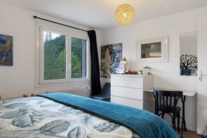 A bedroom with a bed, a desk, a chair, a radiator, and a window with curtains.