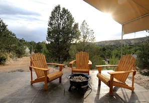 Un patio con tres sillas Adirondack de madera, una parrilla negra con albóndigas y vistas a un paisaje montañoso.