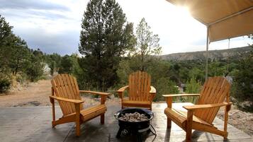 Eine Terrasse mit drei Holz-Adirondack-Stühlen, einem schwarzen Grill mit Hackbällchen und Blick auf eine gebirgige Landschaft.