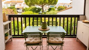 A balcony with a table and chairs, a potted plant, and a view of a tree and buildings. - Casa Arletta | 4 people | AC | private parking | free Wi-Fi | beaches within walking distance (Les saintes maries de la mer)