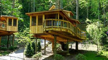 Two wooden treehouses with balconies, set in a forested area.