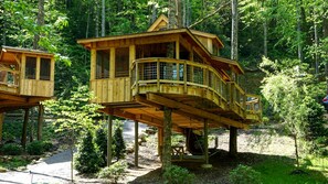 Twee houten boomhutten met balkons, gelegen in een bebost gebied.