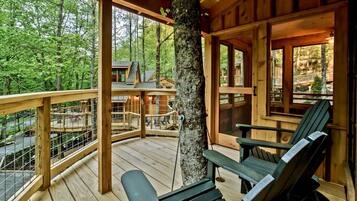 A wooden deck with a view of a forested area, a tree trunk, and a chair.