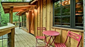 A wooden cabin with a deck, a table, and two chairs.