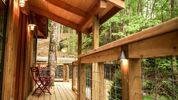 A wooden deck with a railing, a table with chairs, and a view of a forested area.