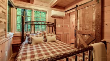 Een slaapkamer in een houten chalet, met een bed, kussens, een raam en een airconditioning.