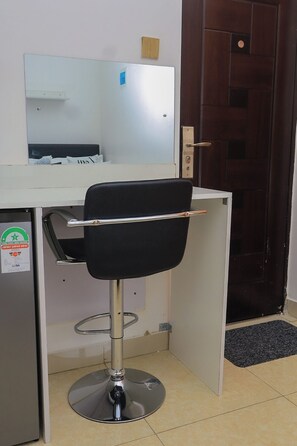 A bar stool with a black seat and chrome legs, a white countertop, a mirror, and a wooden door in the background. - Cosy Studio in a Quiet, Accessible Setting (Nairobi)