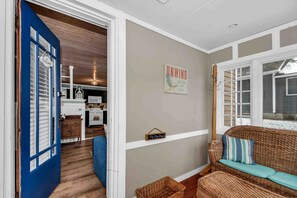 A cozy interior with a blue door, a wicker sofa with cushions, a kitchen area, and a wall with a 'Welcome' sign. - Wonderful Secluded Cottage Close to Lake Michigan in New Buffalo, Michigan (Grand Beach)