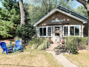 Een klein gebouw met een bord waarop 'Beach House' staat, en twee blauwe Adirondack-stoelen ervoor.