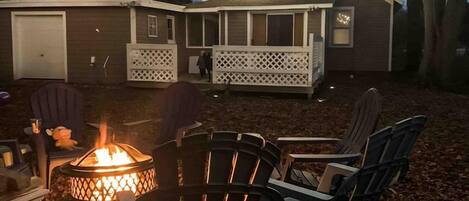 A backyard with a fire pit, outdoor seating, and string lights.