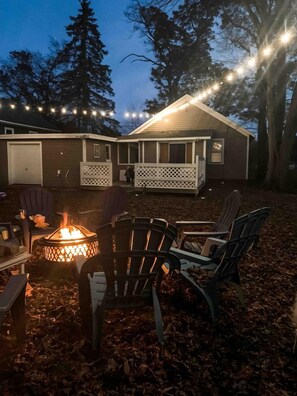 Een achtertuin met een vuurkuil, buitenmeubilair en sfeerverlichting.