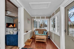 A cozy living room with a fireplace, a television, a blue sofa, and a wicker sofa with cushions. - Wonderful Secluded Cottage Close to Lake Michigan in New Buffalo, Michigan (Grand Beach)