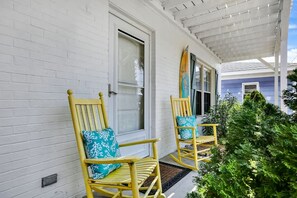 Eine Veranda mit zwei Schaukelstühlen, einer weißen Backsteinmauer und einem kleinen grünen Busch.