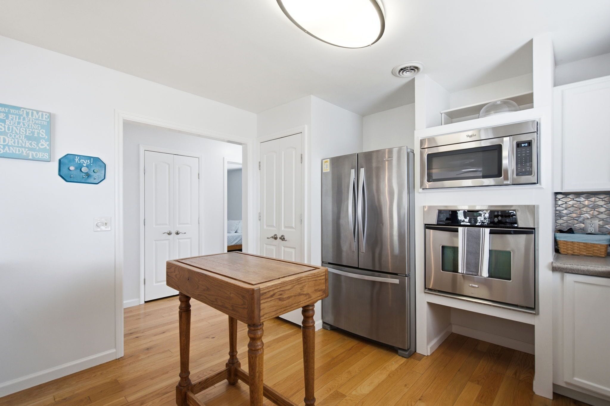 Una cocina con electrodomésticos de acero inoxidable, una mesa de madera y muebles de cocina blancos.
